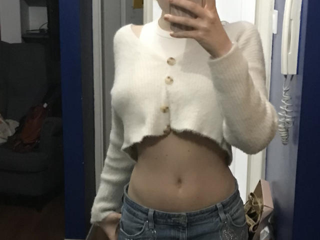 GeorginaClassy wearing a fluffy white crop top with buttons, exposing her midriff and jeans, holding a phone in front of her face, mirror selfie.