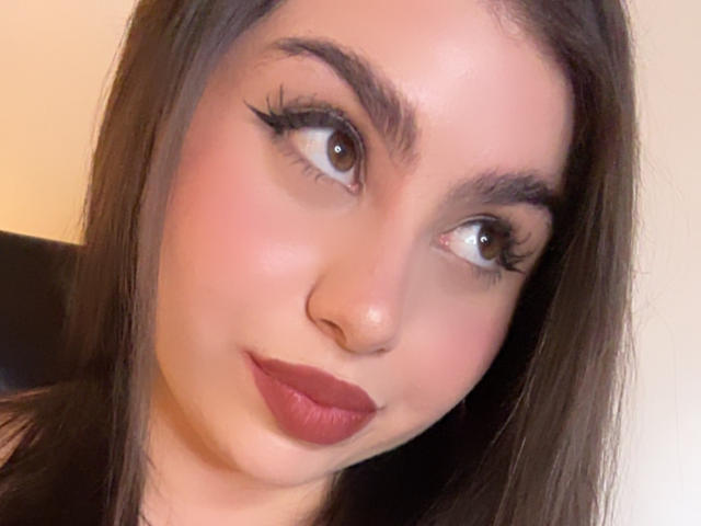 VenusxMusa has brown eyes, thick eyebrows, long eyelashes, and red lipstick, with straight brown hair and a slight smile. Her nose is small and her skin is fair.