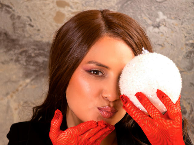 Isabel Soler, met rode handschoenen van gaas, houdt een witte, pluizige spons voor haar oog, met een frons en glanzende, roze lippen, bruin haar en subtiele make-up, voor een ruwe stenen muur..