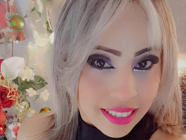 ObedientAndSexy has gray hair, black eyeliner, purple eyeshadow, pink lipstick, and is smiling with bright eyes. Boobs not visible, but has a cute and sexy face.