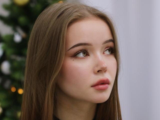 ViolettaFane has long brown hair, light skin, and full pink lips. Her green eyes look to the side with a small beauty mark near her right eye.