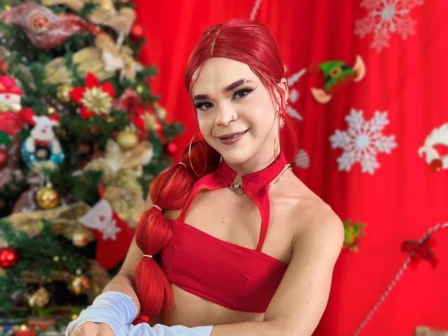 TrioPecadoVipX with red braids, red halter top, showing her tits, smiling, wearing white gloves, Christmas tree in background, red curtain, white snowflakes, and green ornaments.