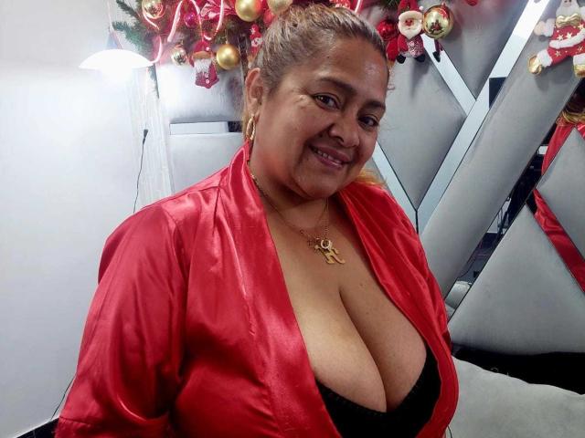 MonzerratBoyer with large tits, wearing a red silky robe, black bra, and gold necklace, smiling, brown hair in a ponytail, Christmas decorations in the background, selfie, curvy.