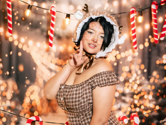 MisakiWong with black hair, wearing a cute reindeer hat, brown off-shoulder dress, and candy cane string lights, flashing a peace sign, showing off her big, round tits.