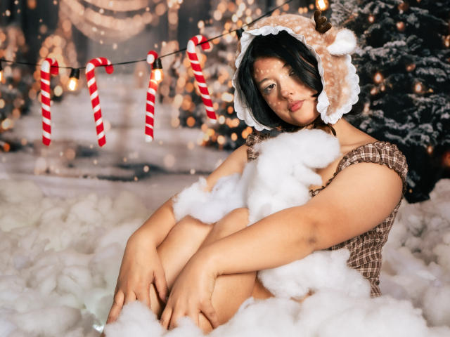 MisakiWong sitting in fluffy white "snow" with arms wrapped around knees, wearing a cute reindeer hood, and brown checkered top, surrounded by glowing lights and candy cane strings.