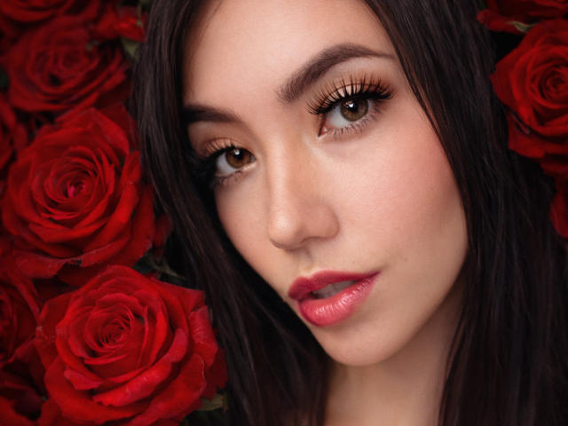 Il viso di Sofie White, con rose rosse, occhi marroni, lunghe ciglia, labbra rosa e capelli castano scuro, che guarda leggermente di lato, con un'espressione dolce e naturale..