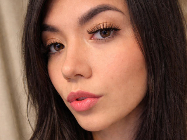 Close-up of SofieWhite's face. She has light brown skin, dark brown eyes with long, thick eyelashes, and full pink lips. Her straight, dark brown hair frames her face. The image has a soft, natural light highlighting her facial features. Her eyebrows are thin and slightly arched. The texture of her skin is smooth with subtle, natural skin tones. The focus is on her face, with no visible background. The overall composition is centered and balanced.
