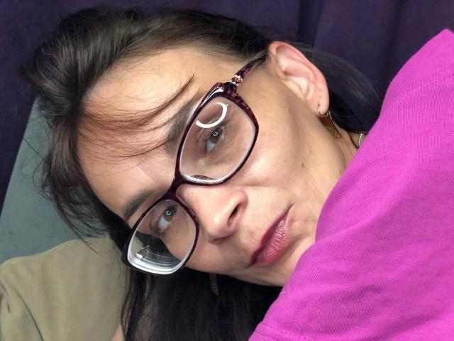 DarkOpiumX-hot with glasses, lying down, pink shirt, dark hair, slight smile, ear earring, reflection in glasses, close-up, relaxed expression, medium skin tone, subtle makeup.