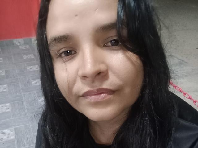 GustaMegan a une peau marron moyen, des cheveux noirs mi-longs et une petite tache de beauté au-dessus de son sourcil droit. Ses lèvres sont légèrement entrouvertes, avec un sourire discret..