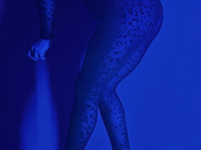 BalletSwan's ass and legs in a blue-lit, leopard-print bodysuit, standing with one hand against a dark wall, showing a strong, curvy, and sexy lower body.