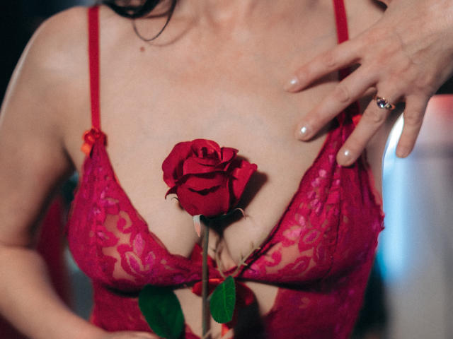 EvanessaJohn's red lace bra, holding a red rose between her tits, with a hand touching her chest, wearing a ring, black hair, and a ring on her finger.