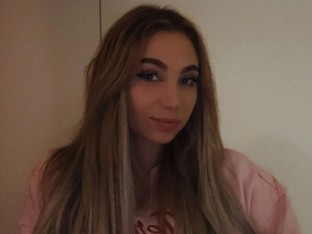 LilyLiebe-hot with long, straight blonde hair, blue eyes, and a slight smile, wearing a pink shirt, looking cute and sexy.