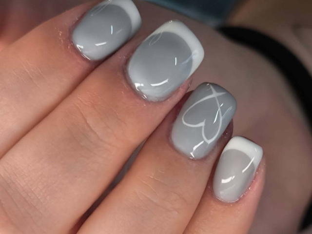 ElvinnaLaFrancaise's nails are glossy gray with white tips, featuring a subtle heart design on the middle nail. Her hand is slightly curved, showing off her manicure.