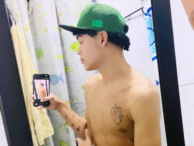 ErikHt, shirtless, wearing a green cap, holding a phone to take a mirror selfie, tattoos on chest and arm, pale skin, short curly black hair, small penis, bathroom.