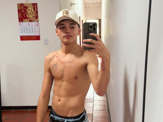 ErikHt is shirtless, wearing a white cap with a gold "E", holding a phone, showing a tattoo on his left chest, and wearing blue underwear in a mirror selfie.