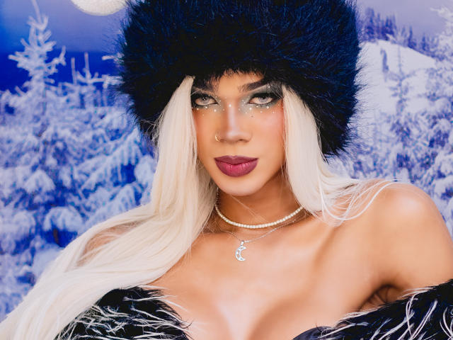 NaomiSteward with blonde hair, black furry hat, glittery eyes, red lipstick, pearl necklace, and black fur off-shoulder coat, showing her tits, in a snowy forest background.