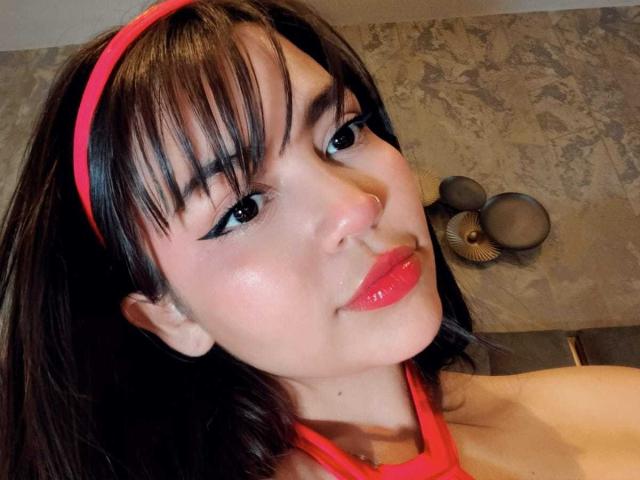 KimDevinne has shiny black hair with bangs, a red headband, and is wearing a red halter top, showing glossy pink lips and a cute nose ring.