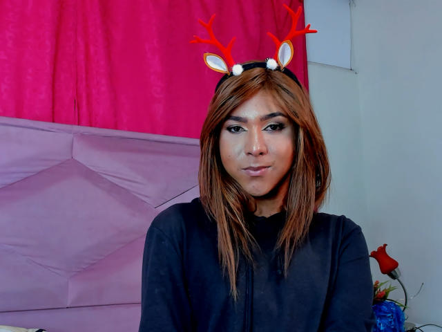 ZoeHotMoretti with brown hair, wearing red reindeer antlers, black shirt, and subtle makeup, pouting slightly, in a room with pink and purple decor.