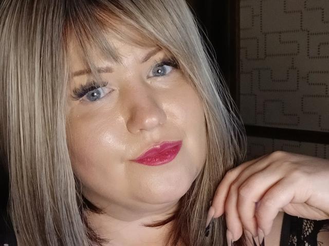 RadaFoxy ha i capelli biondi, gli occhi azzurri e il rossetto rosa. La sua mano, con le unghie curate, è appoggiata vicino al viso. Sta sorridendo leggermente. Il suo seno non è visibile..