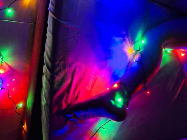 GraceRedMiller's ass, illuminated by colorful Christmas lights, with a focus on her right buttock and a glowing green light near her crotch. Background is dark and blurred.