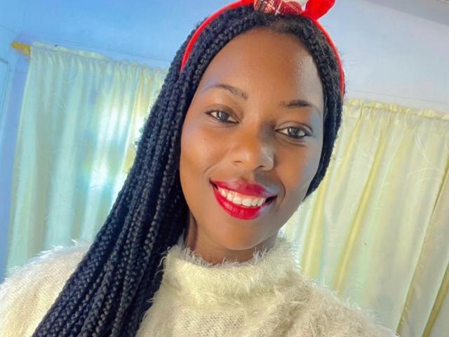 SaraMarks has dark brown skin and long, straight black braids, wearing a red headband with a bow. She has bright red lipstick, a wide smile, and brown eyes. She's dressed in a fuzzy white sweater. The image uses bright, even lighting, emphasizing her facial features and vibrant red lipstick. The overall composition is close-up, focusing on her face and upper body. The style is straightforward and modern.