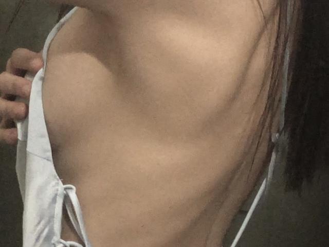 Close-up of Valnes' back and side, showing a thin, muscular, and slightly ribbed torso. Valnes is pulling a white, thin-strapped top down, exposing their right shoulder and upper back. Valnes' light brown hair is partially visible. The skin is smooth with subtle shadows highlighting the contours. The image focuses on the texture and form of Valnes' body. Slight tension in Valnes' hand is visible. The overall composition emphasizes the simplicity and natural beauty of the human form.