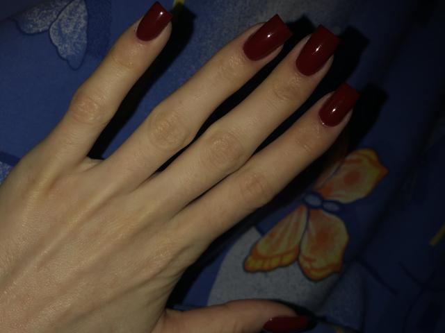 Valnes' hand with shiny red nail polish, showing off long, squared-off nails. Her fingers are slightly spread, displaying smooth, pale skin and a subtle texture.