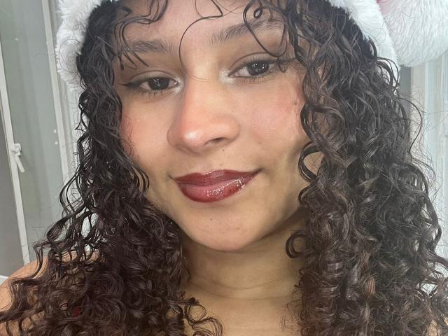 SofiaPassionne has curly brown hair, red lipstick, and a white furry hat, with wet hair and a slight smile, showing a small water droplet on her lower lip.