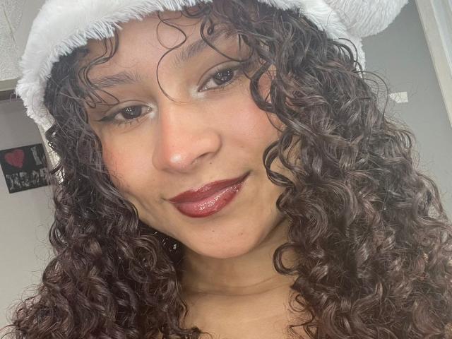 SofiaPassionne has curly brown hair, dark red lipstick, and a white fuzzy hat, smiling with slightly parted glossy lips. Her brown eyes are softly focused.