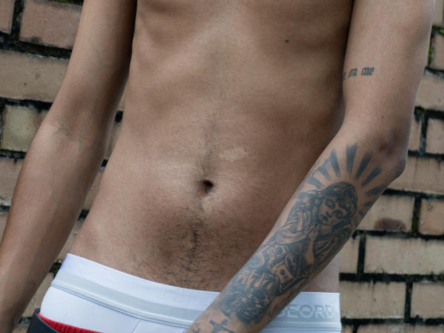 JacobVillalobos' slim, toned, tan-skinned torso with a visible tattoo on his right arm, wearing white underwear, showing a hairy belly and a small navel.
