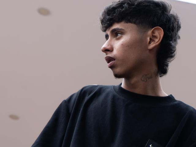 JacobVillalobos with curly black hair, dark skin, small tattoo on neck, side profile, looking to the right, wearing a black shirt, slightly open mouth, casual look.