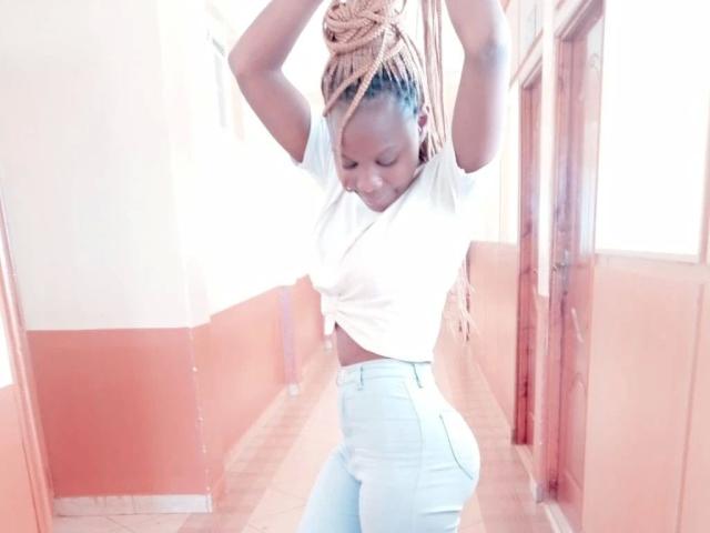 SexxySunflower-hot with braided bun, white tee, and tight jeans, standing in hallway, arms raised, eyes down, wearing a cute, confident expression.
