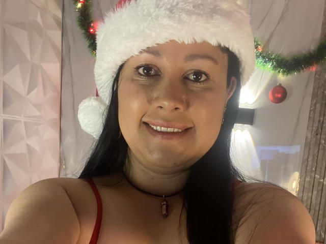 MarianaSmitt, wearing a Santa hat, smiling with brown eyes, black hair, red spaghetti straps, and a necklace, has a cute face and small tits.