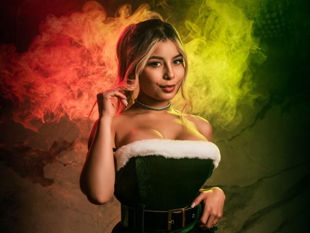 AmaraRicci with blonde hair, green velvet dress, white fur trim, choker, yellow-green-red smoke, hand near face, sexy, cute, soft lighting, medium breast size, confident expression.