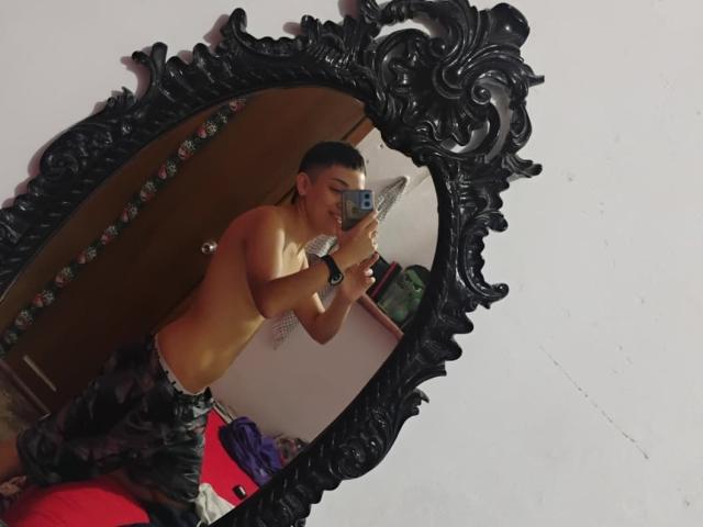 Michaela, oben ohne, hält ein Handy in einem verzierten schwarzen Spiegel, trägt Tarnhose, kurze, dunkle Haare, lächelt, Spiegelbild, Schlafzimmer, Spiegelbild-Selfie..