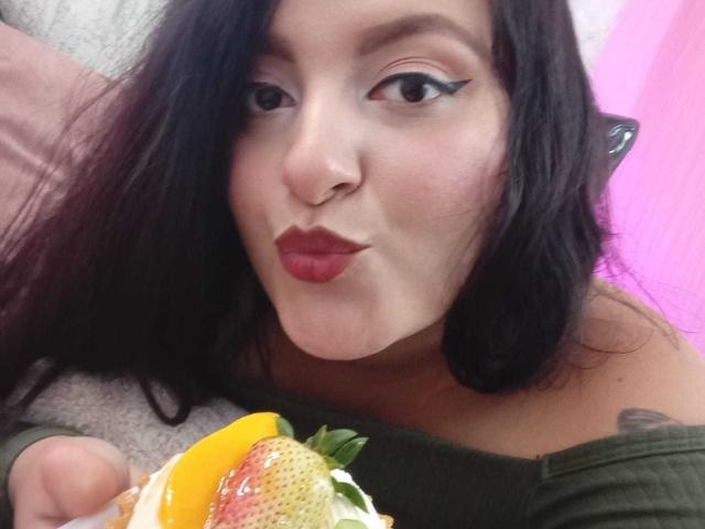 VictoriaRiver with dark hair, red lipstick, and cat-eye eyeliner, pouting her full, shiny lips while eating a taco with lettuce, cheese, and yellow bell pepper.