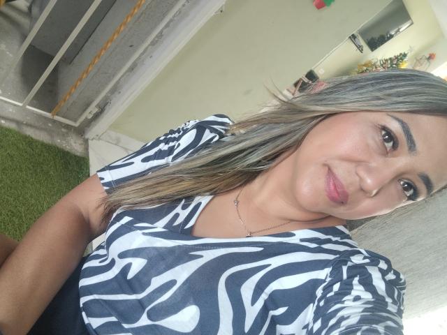 ViolaBertie with grayish-blonde hair, zebra-print top, pink lipstick, and a subtle smile, showing her tits and ass in a selfie. She's wearing a delicate necklace.