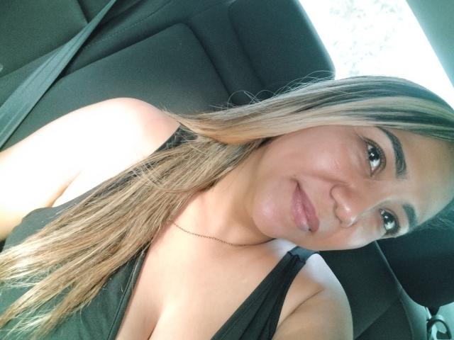 ViolaBertie has blonde-streaked long hair, tan skin, and is smiling with a subtle nose ring, wearing a black top, and sitting in a car with a seatbelt.