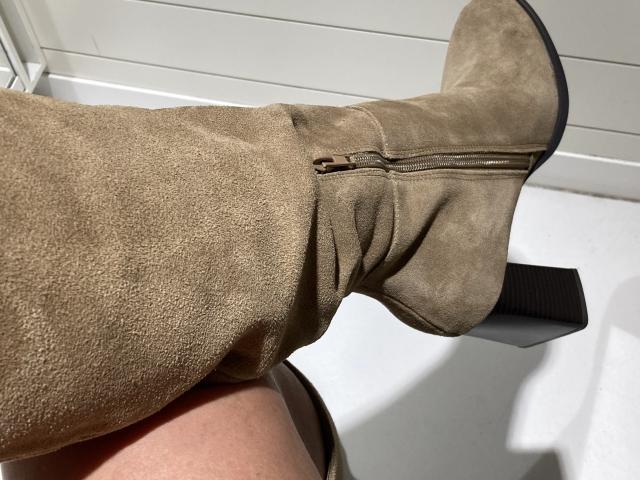 DeesseBleue's brown suede boot with a black heel and zipper, showing a creased upper part, is angled upward in a bright, sunlit setting.