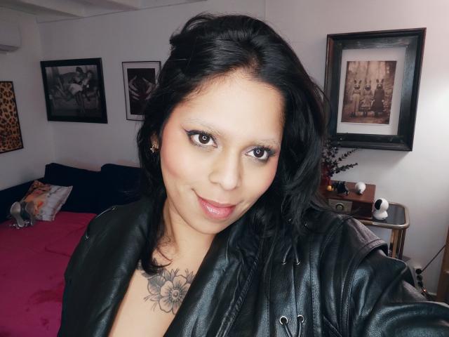 Chili aux cheveux noirs et à la peau claire sourit à la caméra, portant une veste en cuir noir, mettant en valeur un cou floral tattoo.