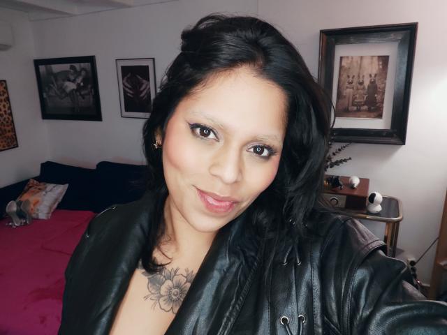 Chili, een solo milf met zwart haar en tatoeages, is het nemen van een selfie in een slaapkamer, het dragen van een zwart lederen jas.