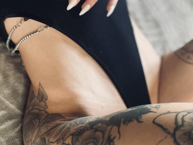 Les culottes noires de DaneeSoHot, qui montrent une cuisse tatouée avec des roses et un bracelet en chaîne, ses longs ongles nude et soignés, et sa peau bronzée et lisse, le tout dans un plan serré et sensuel..