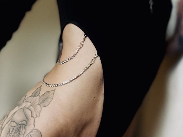 Le côté de DaneeSoHot présente une découpe noire, mettant en valeur deux chaînes en argent délicates et un tatouage de rose sur sa peau pâle et lisse..