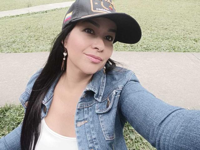 TamaraFoxy, con lunghi capelli neri, indossa una giacca di jeans, una maglietta bianca e un berretto nero, mostra un sorriso carino, ha un piccolo piercing al naso e orecchini pendenti, e sta scattando un selfie..
