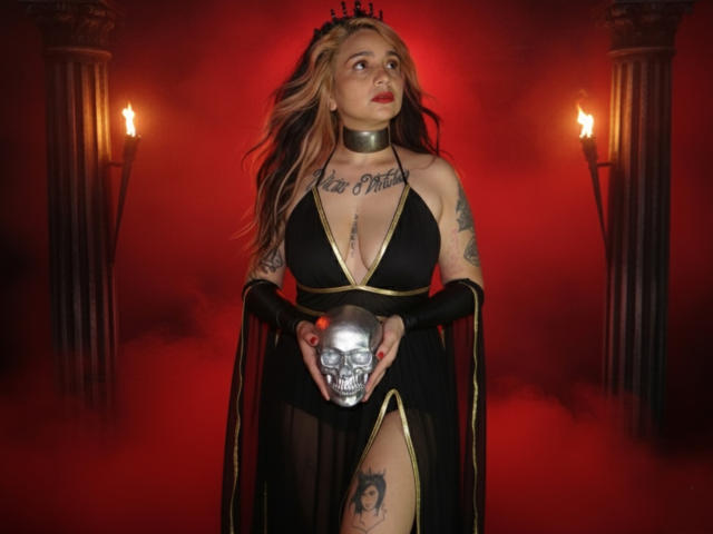 Alexandrapsique with blonde hair, black crown, tattoos, deep cleavage, black dress, gold trim, holding skull, red mist, black arm sleeves, torches, looking up. Boobs, tattoos, skull.