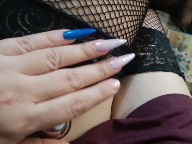 AlinaMistress's hand with long, glossy nails (blue, pink, white) on her black fishnet-covered pussy and lace-clad thigh. Visible pink skin and maroon cloth.