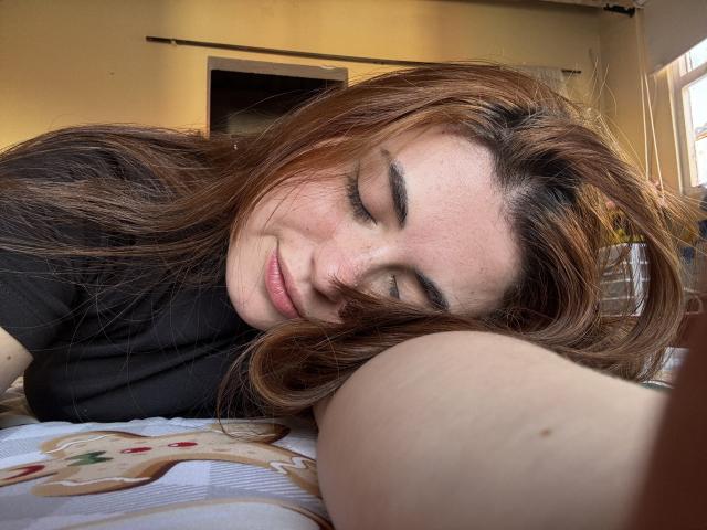 VicluX, a cute girl with brown hair, sleeps with eyes closed, black shirt, freckles, and a gentle smile, laying on a bed with a cookie-patterned sheet.