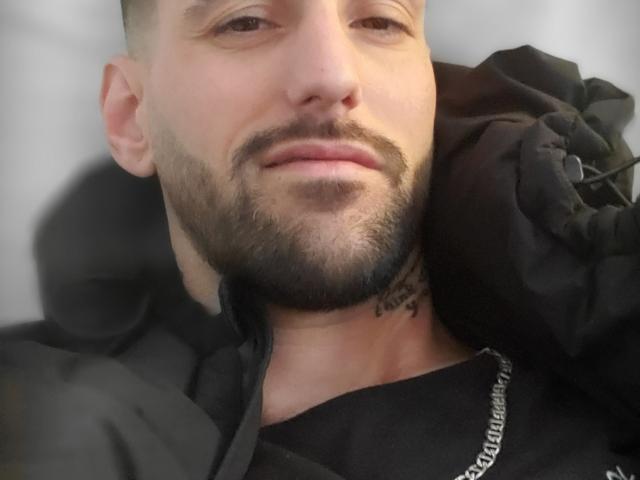 Il viso di BeauDom, leggermente sorridente e con una barba corta, indossa una felpa nera, ha un piccolo tatuaggio sul collo e una collana a catena, è sdraiato con un'espressione rilassata..