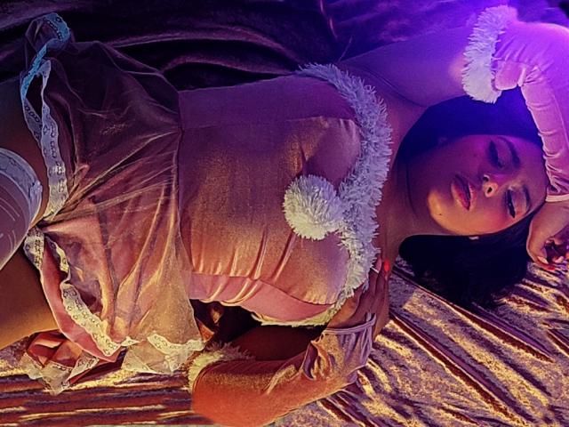 Paola Lyon è sdraiata, indossando un abito rosa, trasparente, in velluto, con pizzo bianco e bordi vaporosi. Ha dei guanti bianchi e tiene gli occhi chiusi. Il suo seno è visibile..