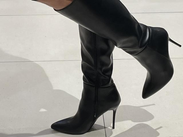 DeesseBleue's black, high-heeled, thigh-length, shiny leather boots with pointed toes and zippers, standing on a white floor with shadows.